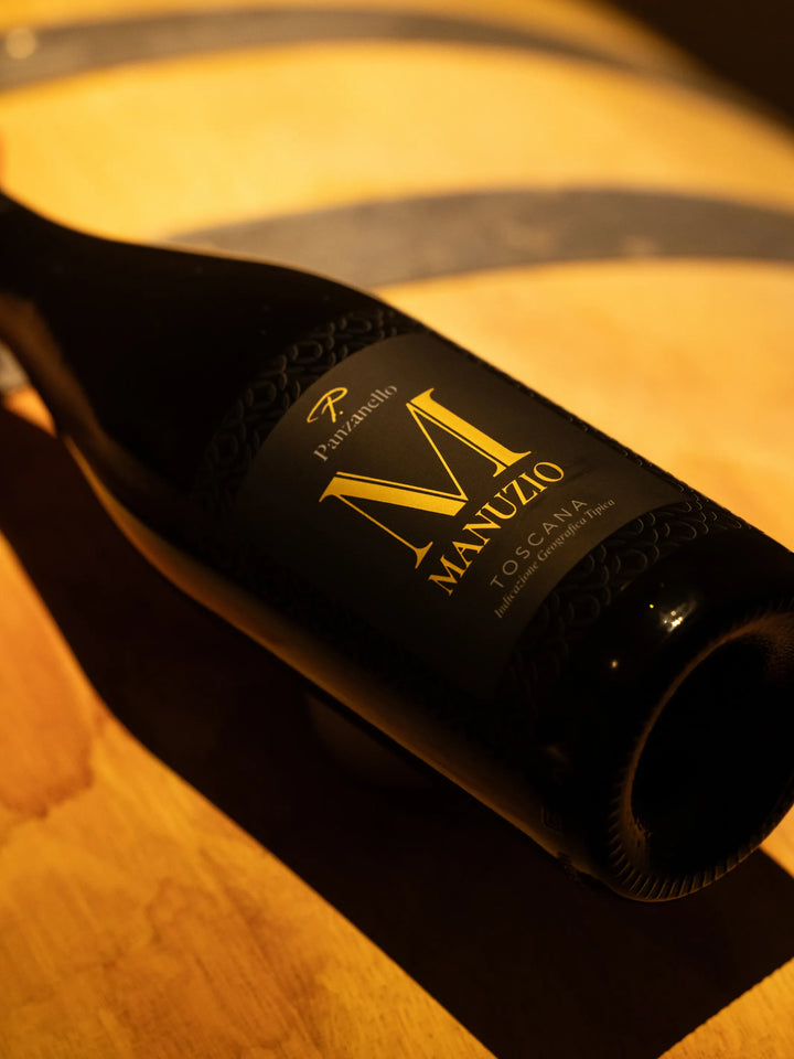 Manuzio Supertuscan Panzanello 2020 disteso su tavolo in legno in agriturismo, vino rosso IGT potente e strutturato 24 mesi in barrique