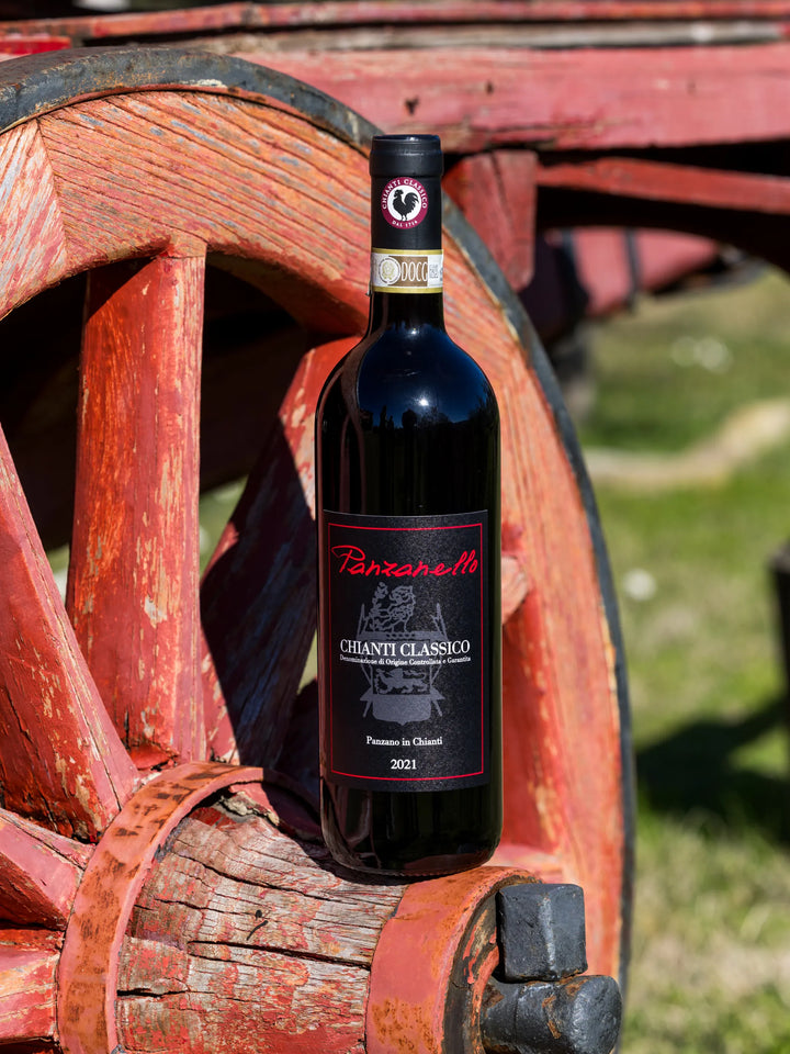 Panzanello Chianti Classico 2022 appoggiato su ruota di carro nella splendida tenuta di Panzano in Chianti, vino rosso fruttato e armonico